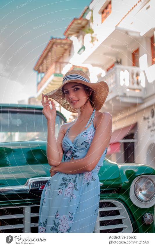 Cheerful young woman in hat standing near retro car on street summer fashion style building portrait smile vacation enjoy vehicle old fashioned vintage female