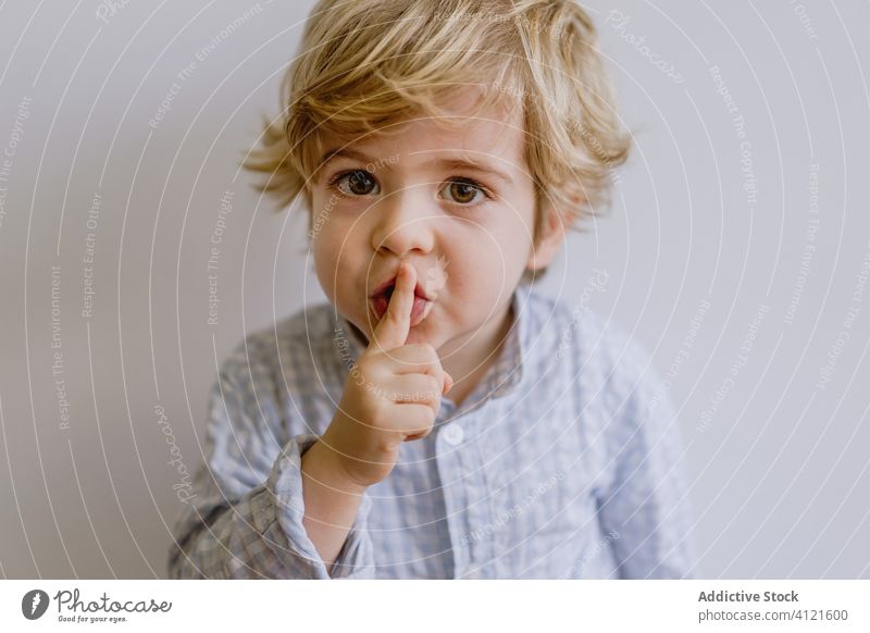 Adorable boy making silence gesture adorable index finger gesticulate little cute kid child content childhood casual face expression happy stand touch lips