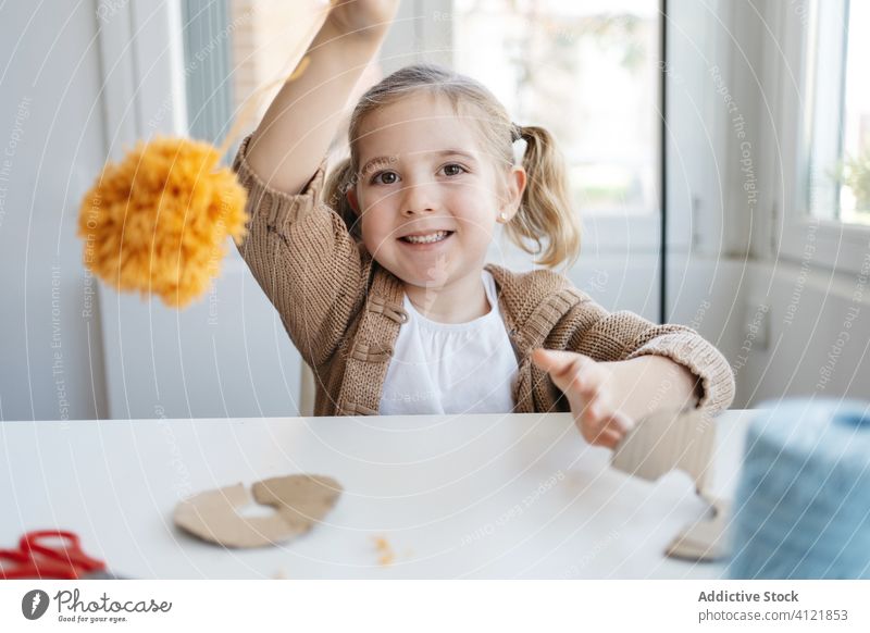 Cheerful small child playing with soft handicraft at light home cheerful girl pompom happy handmade pompon create little studio hobby knitted smile kid creative