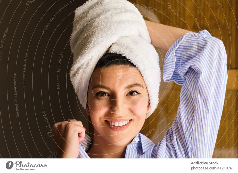 Happy woman with towel on head after bath at home toothy smile shower fresh clean happy morning hygiene lean on hand relax comfort sunlight apartment cheerful