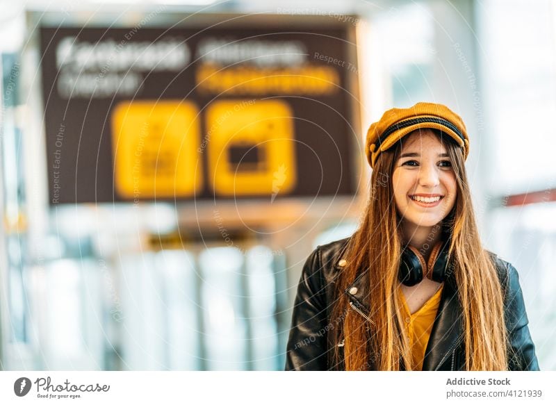 Trendy young woman in modern airport terminal tourist trendy passenger cheerful headphones style fashion departure smile trip handle wait black leather jacket