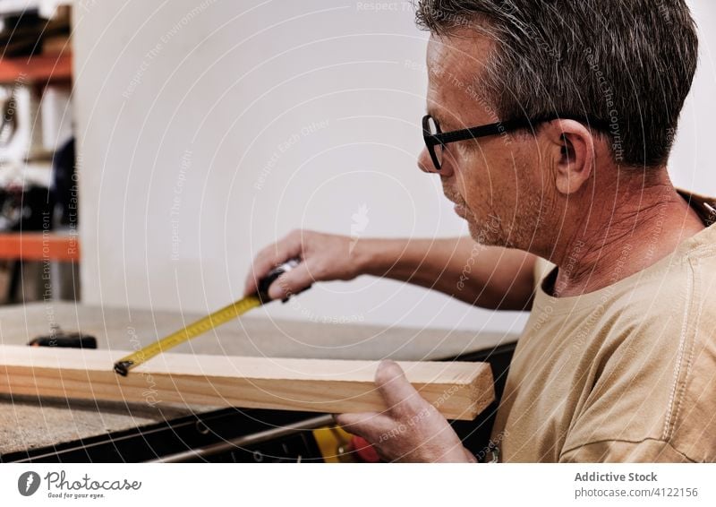 Attentive craftsman using measuring tape while working with lumber in carpentry studio worker control attentive tool precise detail handyman timber wood size