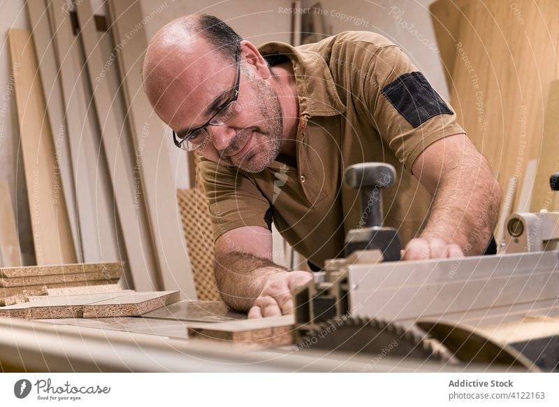 Diligent woodworker cutting lumber using trimming machine in workroom workplace carpentry measure attentive man saw control detail timber joiner master craft