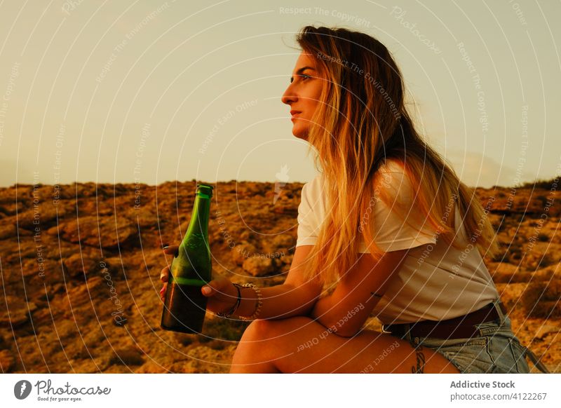 Young lady with bottle of beer during sunset on seashore woman traveler smile refreshment summer chill leisure happy ibiza spain sunglasses drink vacation