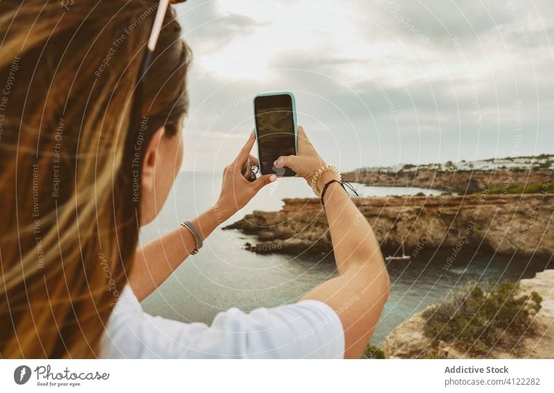 Anonymous female tourist taking photo with smartphone of rocky Ibiza shoreline woman take photo seashore cloudy nature cliff journey coast spain ibiza trip