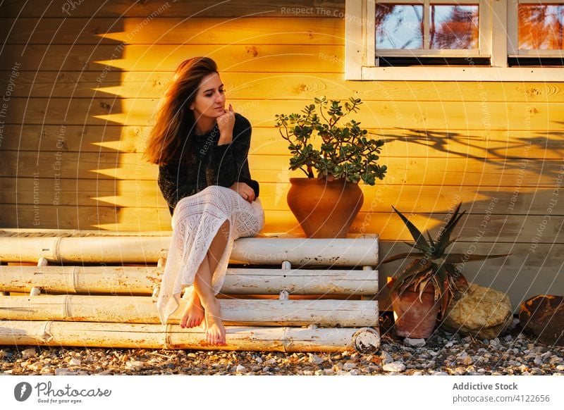Serene woman relaxing on bench near house sunset serene barefoot wooden chill weekend countryside female cozy outfit rest tranquil calm sit peaceful idyllic