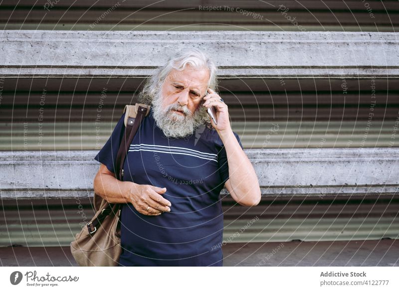 Aged traveling man using smartphone on street traveler aged search information city cellphone male tourist elderly long hair gray hair senior casual wear