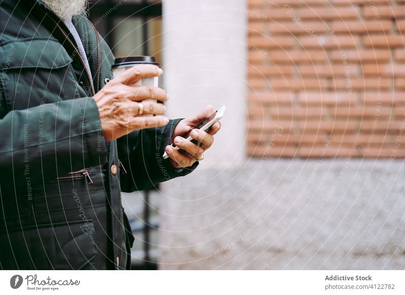 Aged man with takeaway coffee using smartphone during stroll aged browsing street male hot drink senior elderly refreshment city beverage paper cup to go old