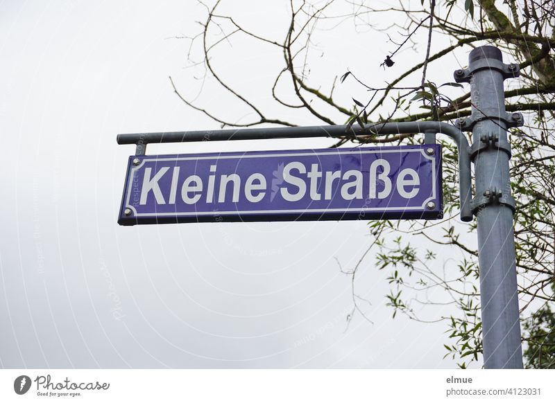 blue street sign " Kleine Straße " on a metal pole in front of a tree / street name small road Metal post Tree Signs and labeling Letters (alphabet) Signage