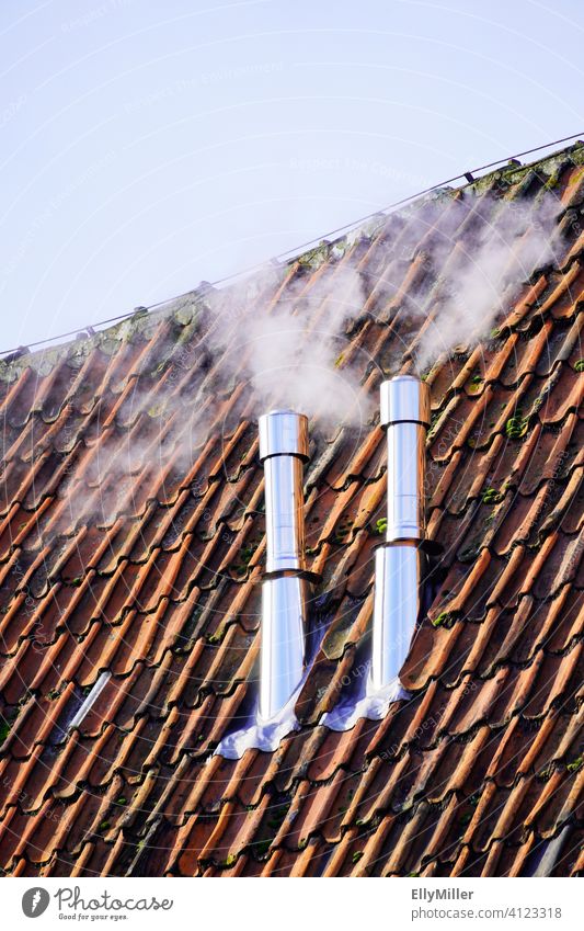 Two smoking chimneys on an old roof with red tiles. Chimney Smoke Roof Heat Warmth Energy warming heat generation smoke High-grade steel Roofing tile Red
