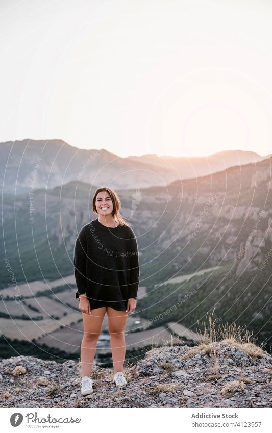 Positive young female traveler standing on cliff in mountains during sunset woman laugh rock smile stone nature vacation journey adventure freedom sky tourism