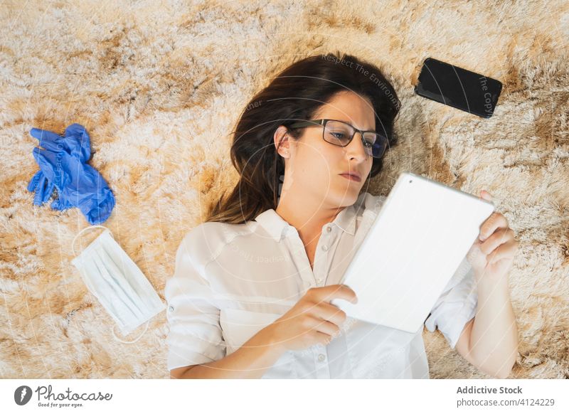 Young woman with protective mask and gloves using tablet coronavirus stay at home work lying bed female serious remote gadget device safety covid covid 19