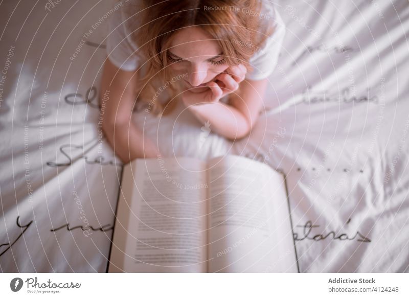 Lazy young ginger woman with book on bed in weekend peaceful lazy dream relax read be my love female lying stomach redhead red hair white t shirt romantic decor