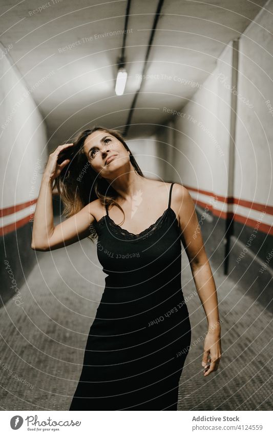 Happy woman in black dress standing in corridor passage enclosure dream underground concept restrict confine smile young female inside isolation think building