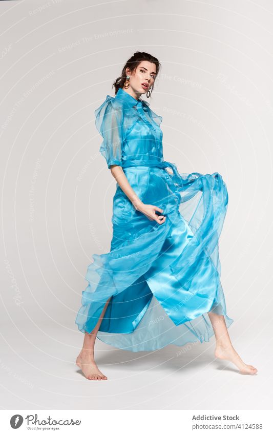 Young stylish lady in blue dress standing in studio and looking down woman style fashion vogue posing attractive long hair young trendy color transparent fabric