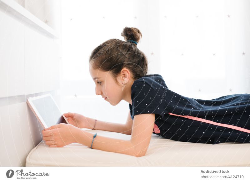 Positive girl using tablet while resting on bed at home browsing social media teen chill positive relax pajama internet bedroom comfort device gadget connection