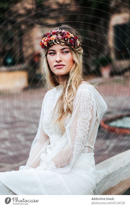 Blond bride resting in yard woman wedding dress wreath flower young elegant female translucent floral serene event celebrate sit tranquil calm peaceful blossom