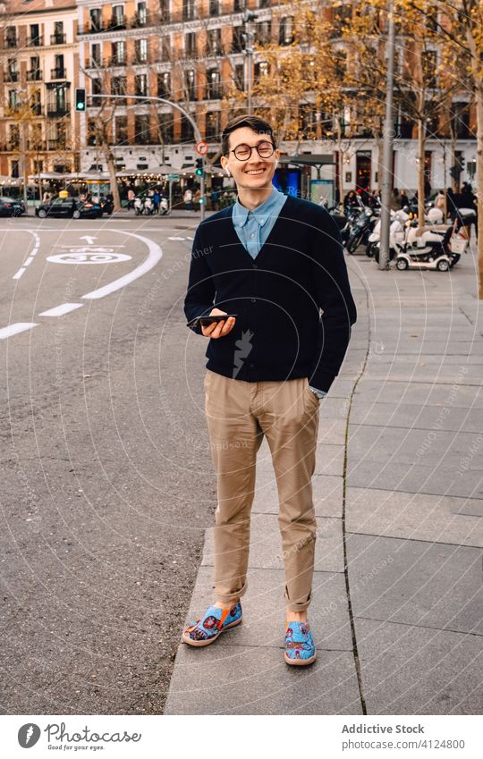 Stylish young man standing on sidewalk with smartphone trendy style street fashion confident music eyeglasses earphones city outfit device outdoors listen