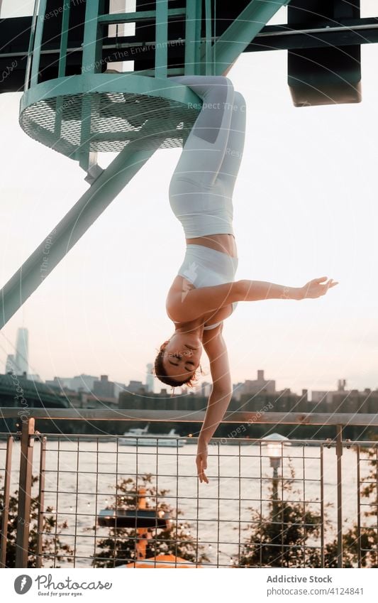 Graceful woman hanging upside down in city meditate urban industrial tranquil cityscape grace sportswear balance female slim serene calm quiet eyes closed relax