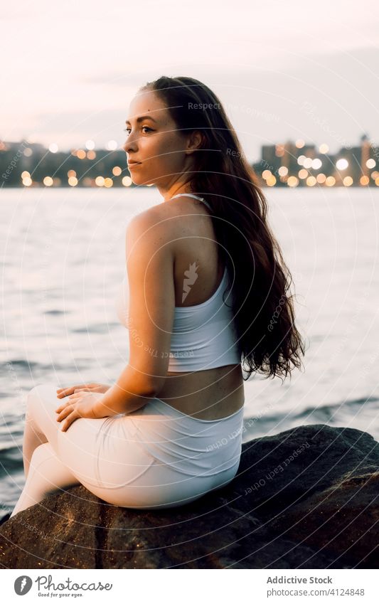 Calm woman in lotus pose on rocky coast of river cityscape stone waterfront practice evening female calm concentrate focus tranquil serene river bank riverside