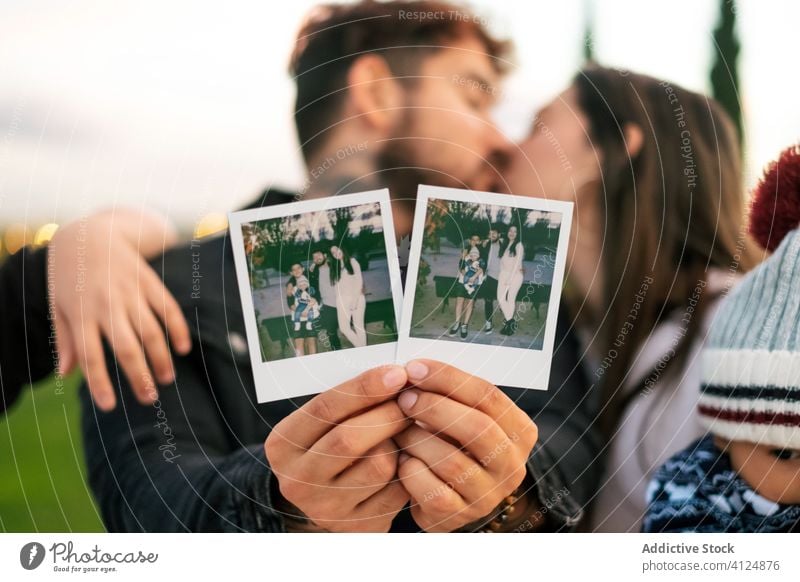 Kissing couple with kids holding family photos kiss love show young picture happy relationship demonstrate photography park parent instant candid optimist