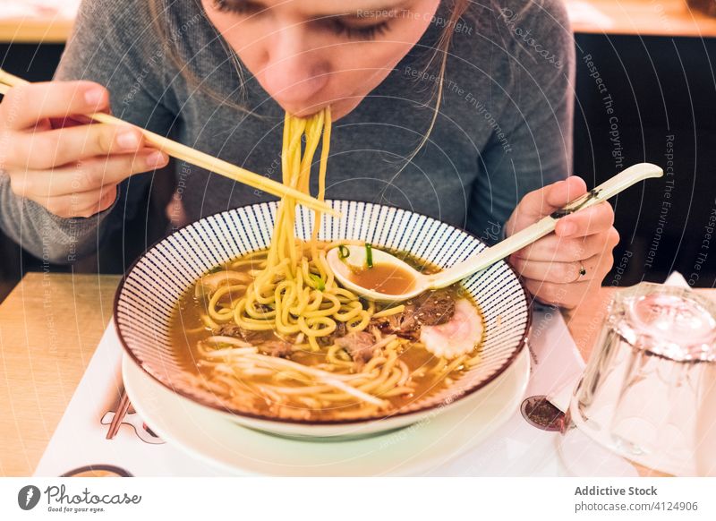 Young woman eating ramen in cafe tradition japanese young spoon chopstick bowl female dish table tasty cuisine lifestyle restaurant food meal delicious asian