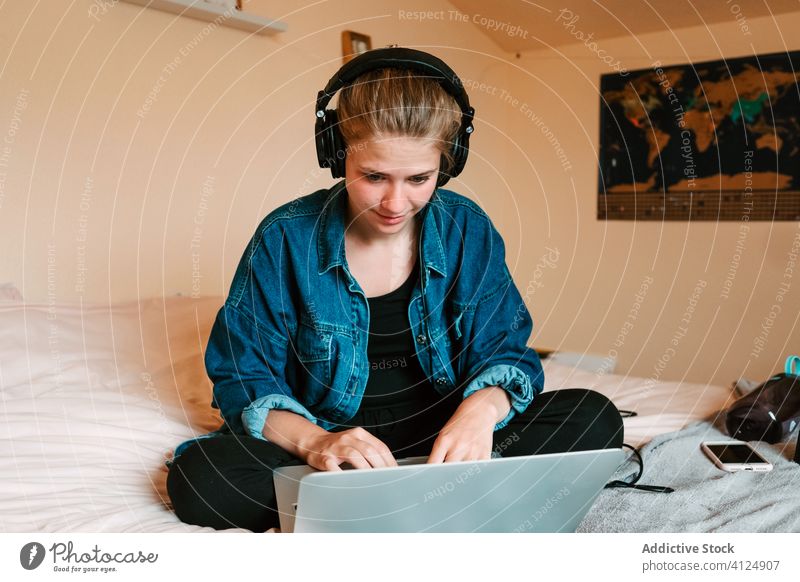 Cheerful young woman using laptop in light bedroom at home headphones read surfing social media watch relax chill listen search lounge check joy rest browsing