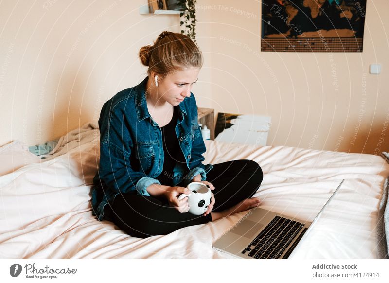 Woman watching movie while having hot drink and using laptop in cozy bedroom woman home cup surfing social media listen female beverage interest film earphones
