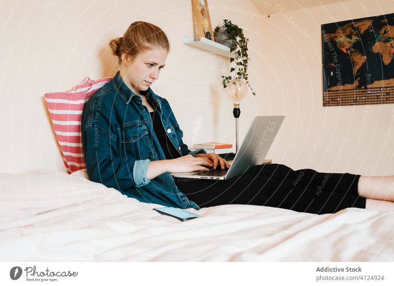 Young woman using computer while chilling in light bedroom laptop home use relax foot barefoot social media watch browsing surfing mail female search read