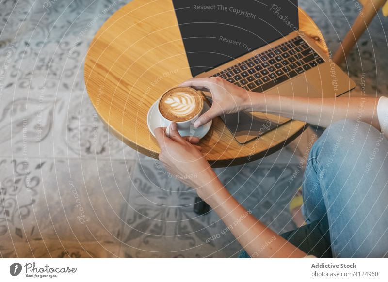 Adult woman drinking aromatic coffee while working on laptop at home freelance using cafe foam internet latte cup beverage cappuccino surfing browsing read