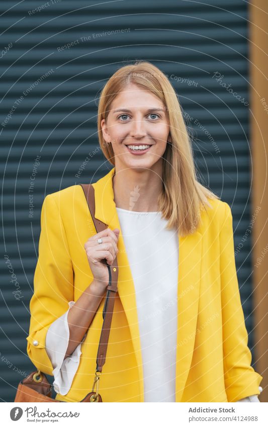Joyful stylish woman with handbag over shoulder on street jacket smile joy fashion outfit blond happy charming satisfied freelance style female delight apparel