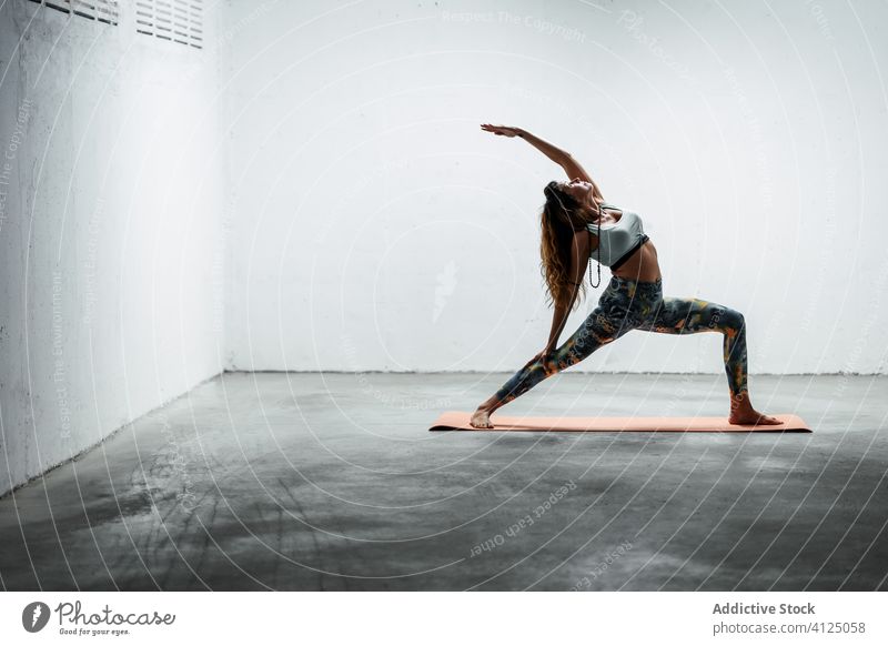 Slender woman doing yoga in reverse warrior pose balance practice calm slender asana female slim mat flexible stand floor sportswear leggings bra fit lady