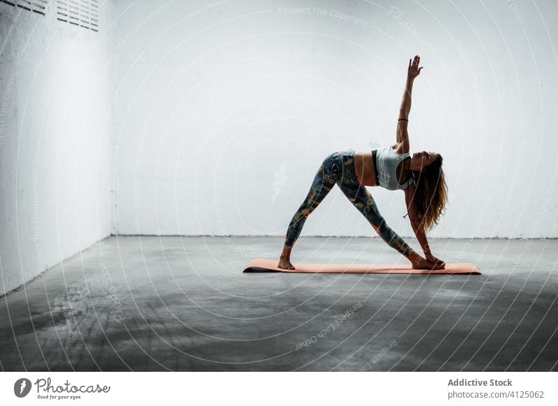 Slender woman doing yoga in extended triangle pose balance practice calm slender Utthita Trikonasana female slim mat flexible stand floor sportswear leggings