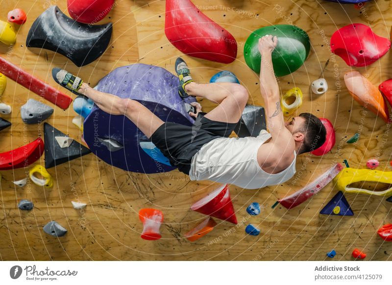 Strong man hanging on wall practicing climbing sport training boulder hobby equipment gym activity workout athlete extreme male strong exercise effort active