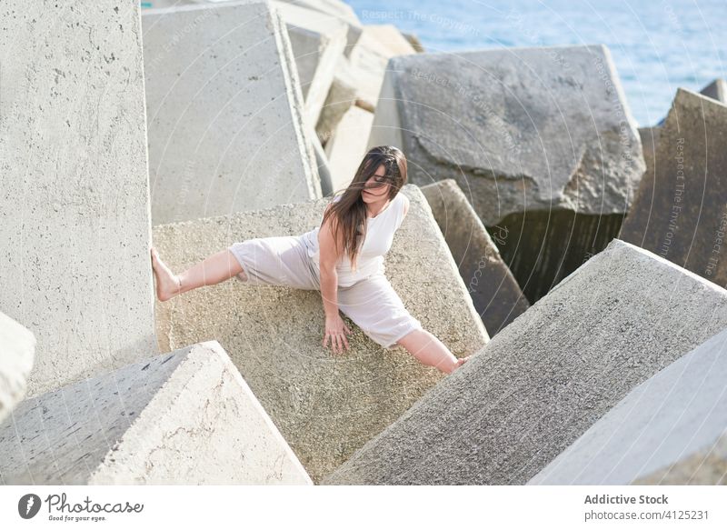 Young woman sitting on stone construction concrete dance sensual power nature harmony contemporary shore coast push modern concept effort young female gray