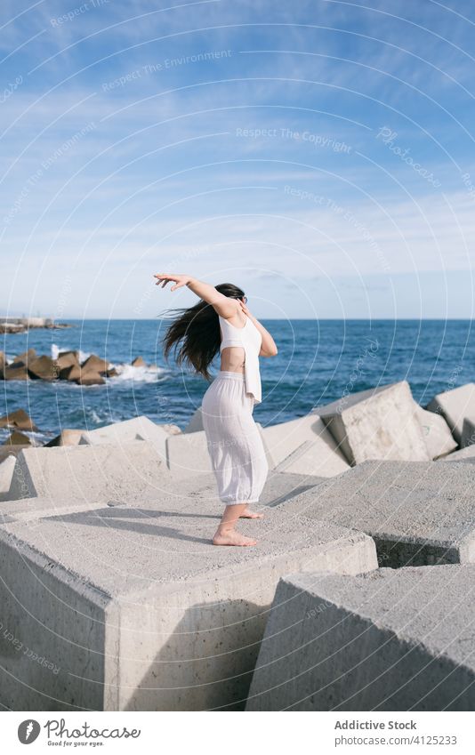 Modern woman standing on concrete block of breakwater sea dance sensual power harmony coast contemporary concept stone construction energy physical young pose