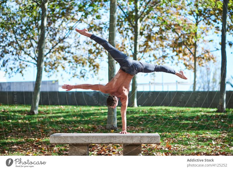 Strong man doing handstand on bench sportsman shirtless stretch balance muscular gymnast strong split muscle fit active body upside down dancer back concrete