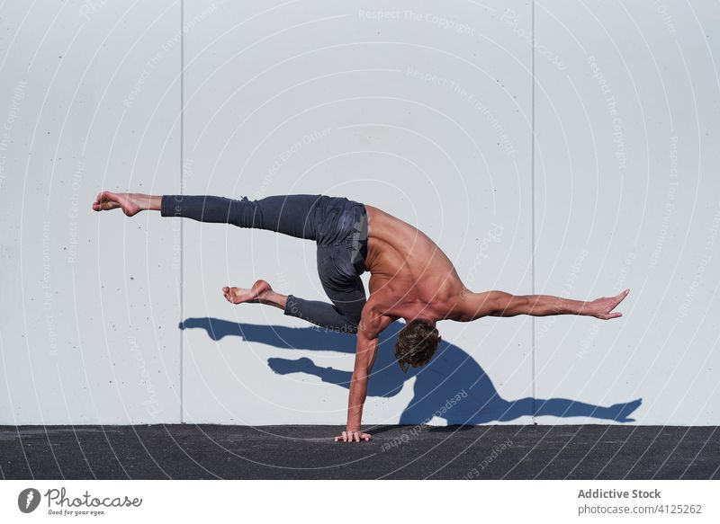 Strong sportsman doing single handstand exercise acrobat shirtless stretch balance muscular strong muscle fit active body back bent knee jeans activity practice