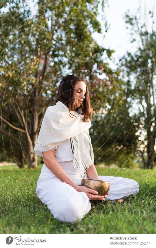 Concentrated young woman with Tibetan bowl in green field yoga tibetan bowl meditate singing bowl asana calm zen lawn pose summer knee tree park harmony