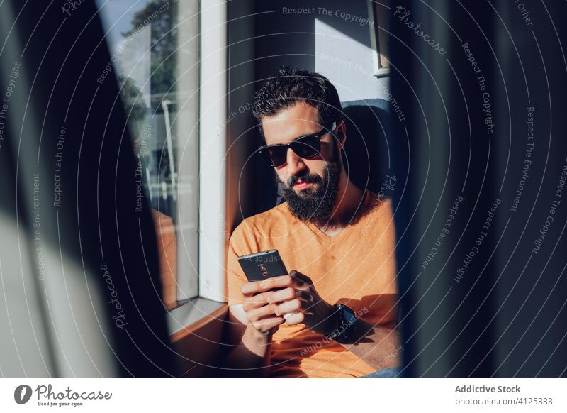 Serious bearded man in sunglasses browsing smartphone in train passenger commute travel summer mobile transport window connection positive young journey