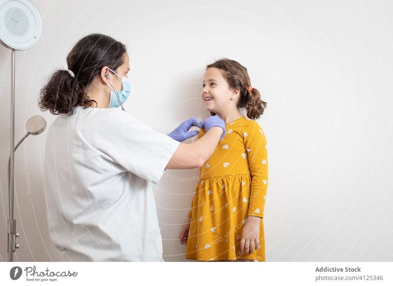 Female doctor examining lungs of little girl in clinic woman mask patient lunge stethoscope hospital glove pneumonia check up covid 19 infection examine virus