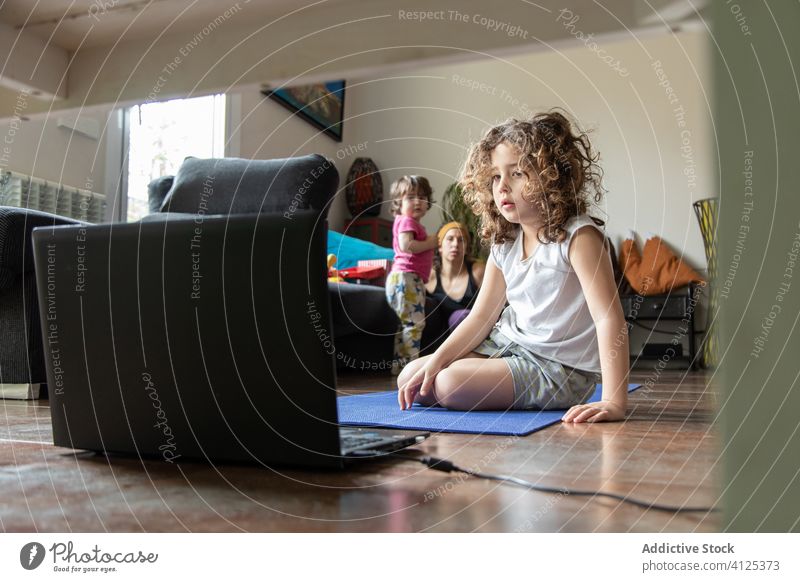 Little girl watching video on laptop during yoga session at home kid online learn practice tutorial device gadget daughter browsing computer communicate