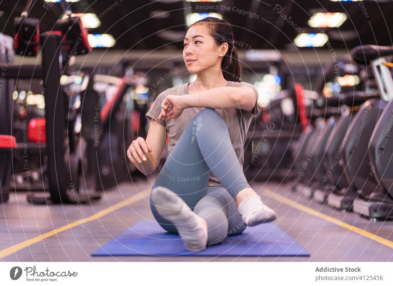Strong young ethnic sportswoman stretching on mat in gym training fitness warm up club slim slender wellness exercise workout athlete sportswear asian healthy