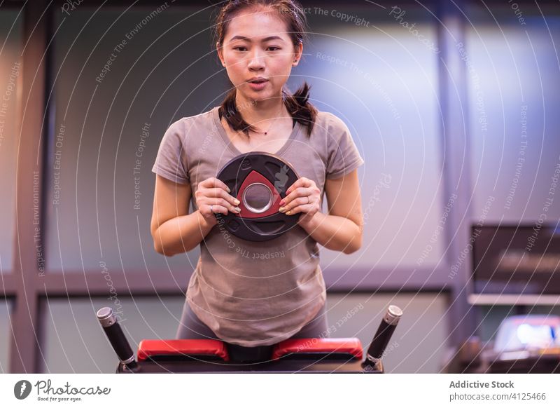 Serious Asian young sportswoman doing exercise with weight on bench in modern gym training hyperextension strong workout athlete active wear wellness body