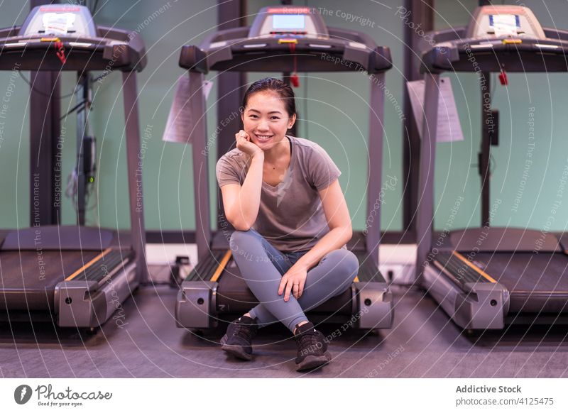 Ethnic sportswoman sitting on treadmill in gym rest break workout cardio recovery cheerful positive active wear fitness young ethnic athlete training happy