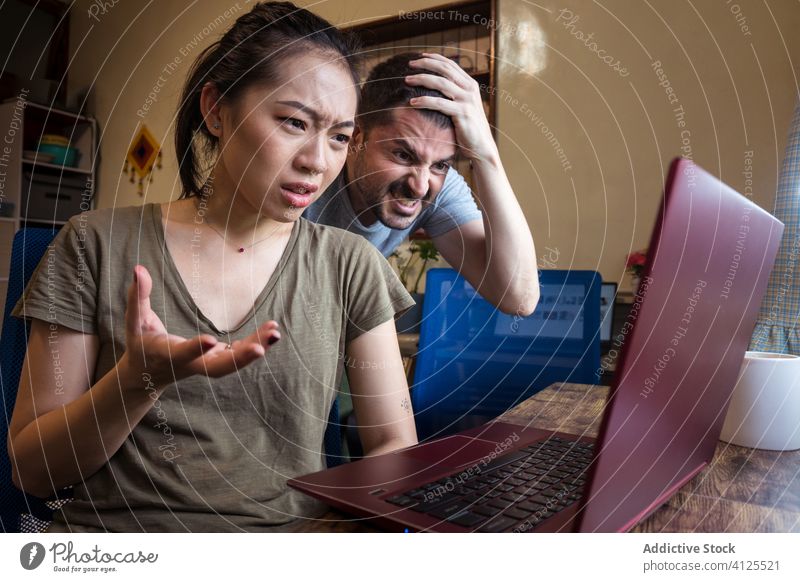 Confused couple of freelancers using laptop together at home confuse problem project work frustrate online multiracial multiethnic diverse asian help