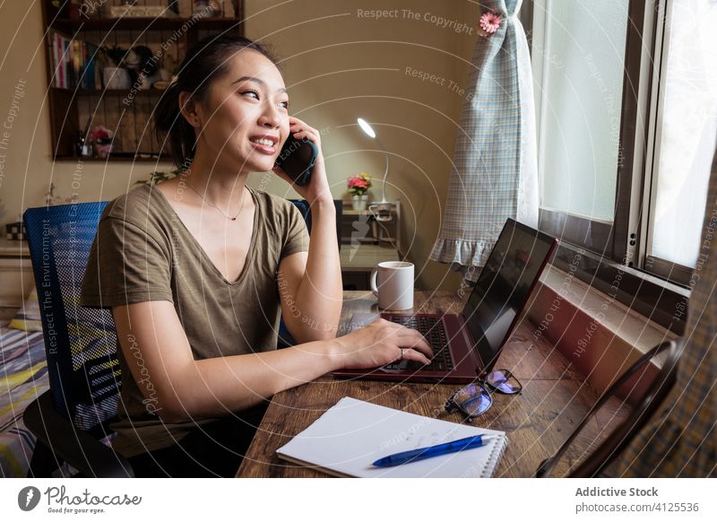 Busy female entrepreneur typing on laptop and using mobile phone smartphone woman home office busy asian ethnic freelance concentrate self employed independent