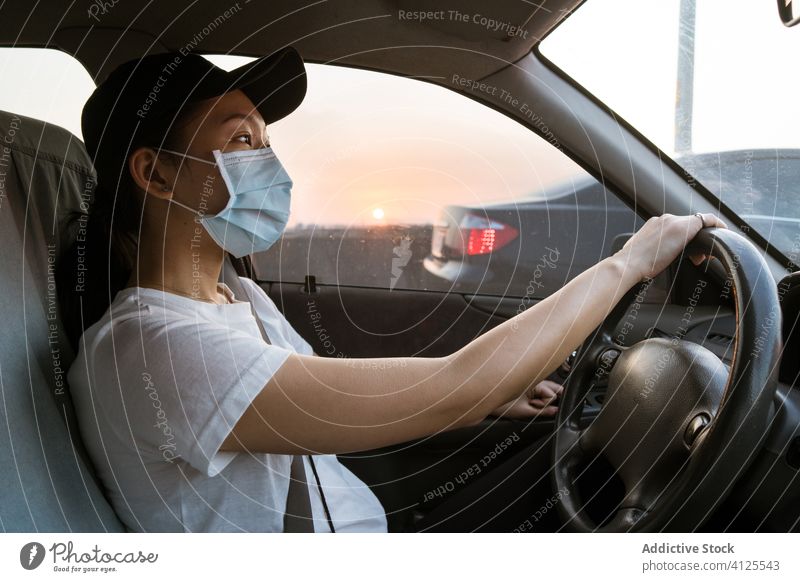 Ethnic woman in medical mask driving car coronavirus drive protect prevent covid young casual automobile trip ethnic asian female modern transport ride safety