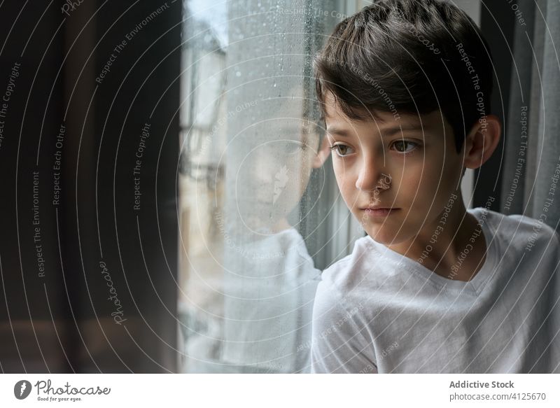 Unemotional boy looking out of window at home bored observe rain living room street unemotional child dreamy kid thoughtful stand lean emotionless serious alone