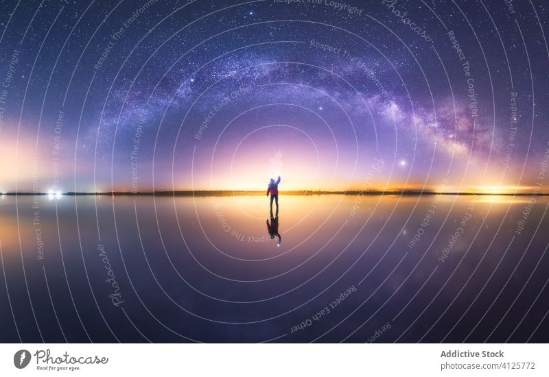 Man among colorful bright stars in dusk man silhouette sky milky way reach out reflection water stand surface light evening night galaxy energy space outer
